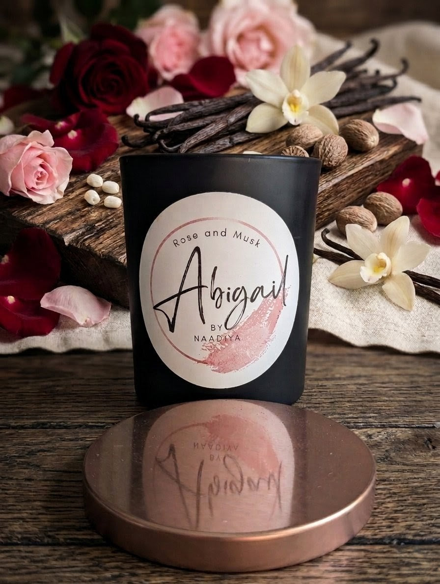 Candle labeled 'Abigail' with flowers and vanilla beans on a wooden surface