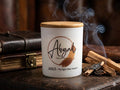 Candle labeled 'Abigail by Naadya' with cinnamon sticks and a leather-bound book in the background