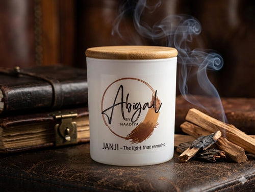 Candle labeled 'Abigail by Naadya' with cinnamon sticks and a leather-bound book in the background