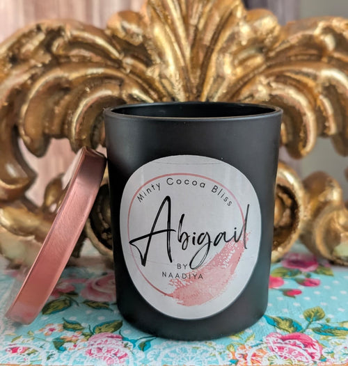 Black candle jar with a decorative label on a floral tablecloth with a gold ornate object in the background