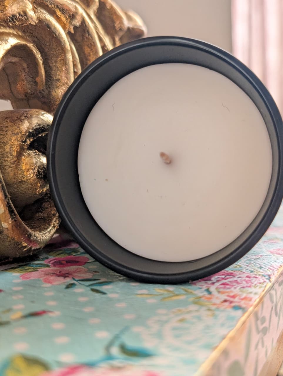 White candle in a black candle jar on a floral surface